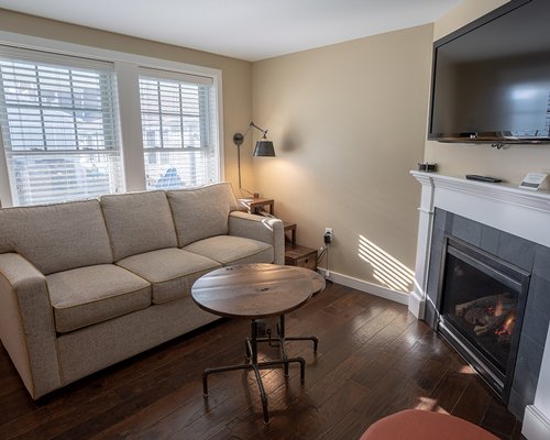 A well furnished living room with a television pull out sofa fire in the fireplace and an outside view.