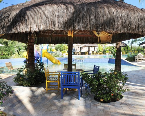 A patio furniture with thatched sunshades alongside a swimming pool with the water feature.