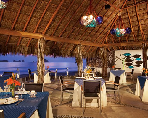 Thatched covered outdoor restaurant alongside the ocean.