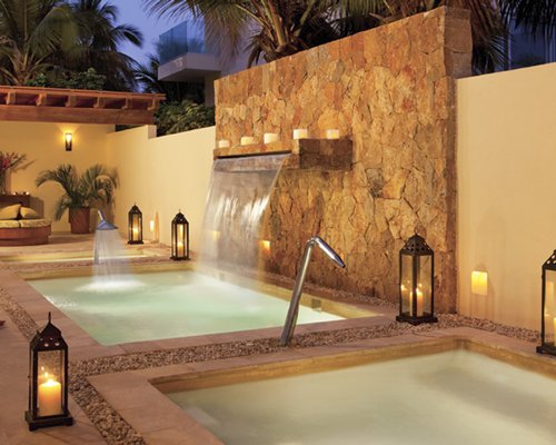 View of two outdoor pool with water feature at dusk.