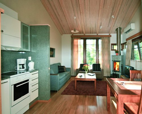 A well furnished living room with a television fireplace and an open plan kitchen with dining area.
