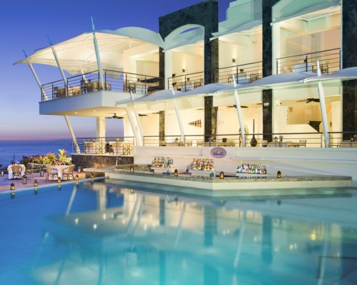 An outdoor swimming pool alongside multi story resort units at dusk.