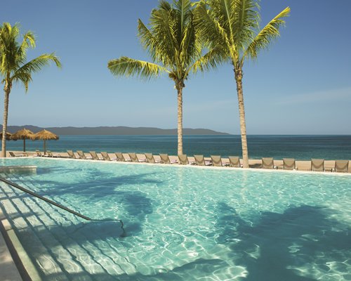 A large outdoor swimming pool with chaise lounge chairs and thatched sunshades alongside the water.