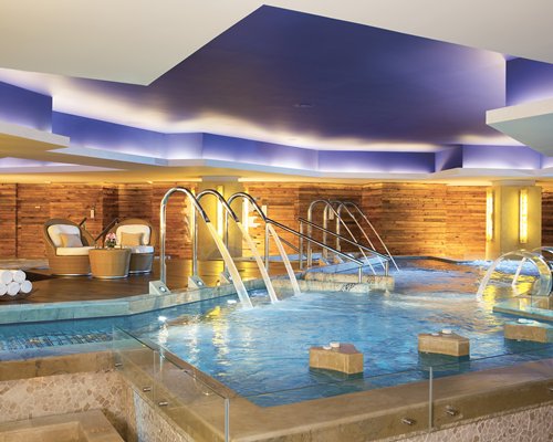 An indoor swimming pool with water curtains and patio furniture.