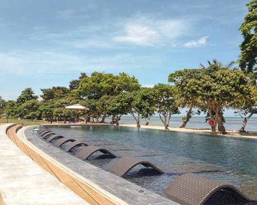 An outdoor swimming pool with chaise lounge chairs and sunshades alongside trees.