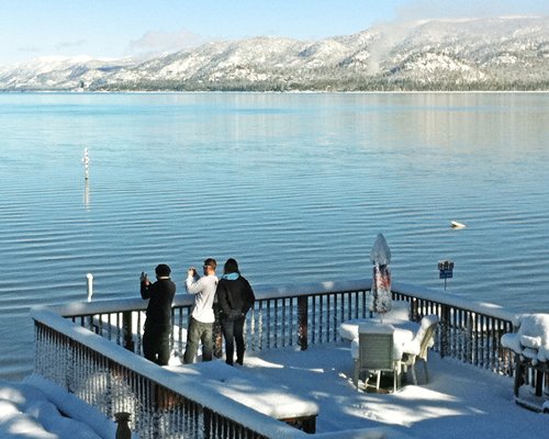 People at an outdoor dining area alongside the lake and mountains.