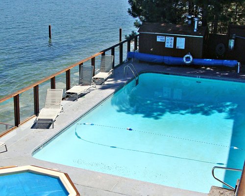 An outdoor swimming pool and hot tub with chaise lounge chairs alongside the lake.