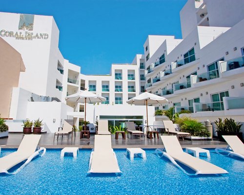 An outdoor swimming pool with in pool chaise lounge chairs alongside resort units.