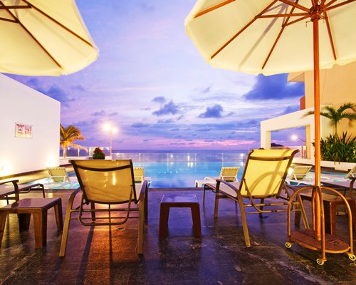 An outdoor swimming pool with chaise lounge chairs and sunshades at dusk.