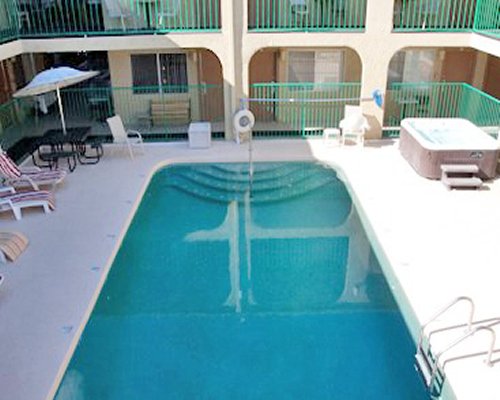 An outdoor swimming pool with hot tub and chaise lounge chairs alongside multi story resort unit.