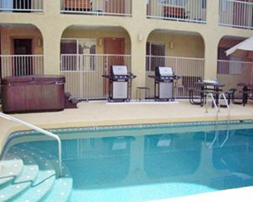An outdoor swimming pool with patio furniture and barbecue grills alongside the resort units.