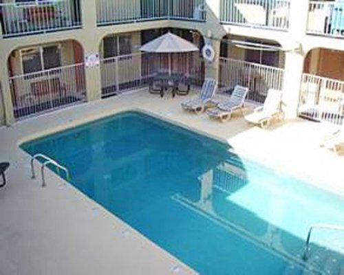 An outdoor swimming pool with chaise lounge chairs alongside multi story resort unit.