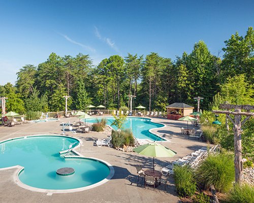 Outdoor swimming pools with chaise lounge chairs and sunshades surrounded by wooded area.