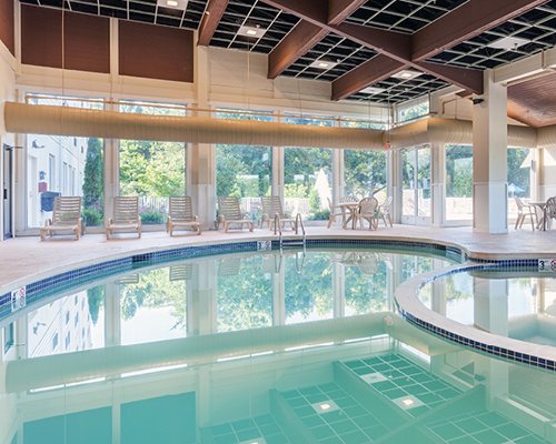 An indoor swimming pool with chaise lounge chairs patio and an outside view.