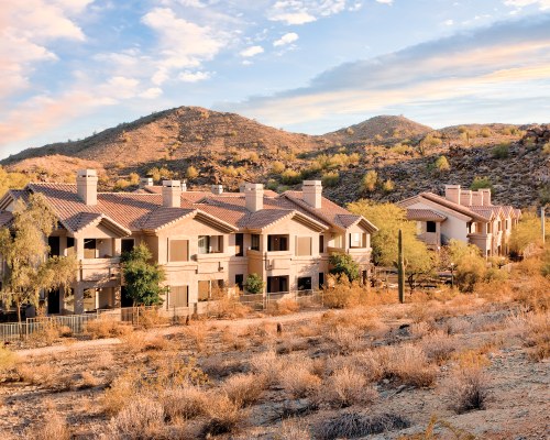 AN EXTERIOR VIEW OF MULTI STORY RESORT UNITS WITH TREES ALONGSIDE HILLS.