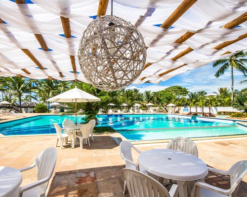 An outdoor swimming pool with chaise lounge chairs patio and sunshades surrounded by trees.