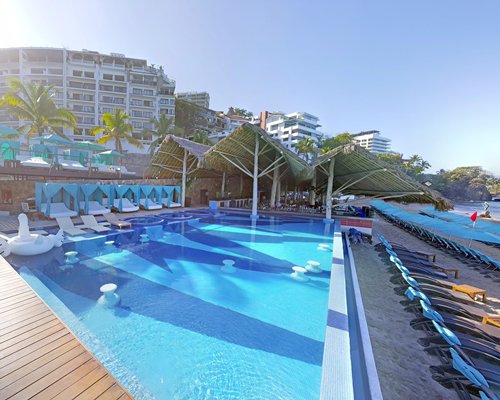 A large outdoor swimming pool with chaise lounge chairs alongside multi story resort units.