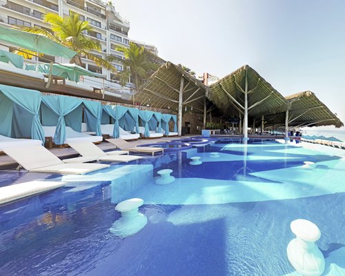 An outdoor swimming pool with a poolside bar and chaise lounge chairs alongside multi story resort unit.
