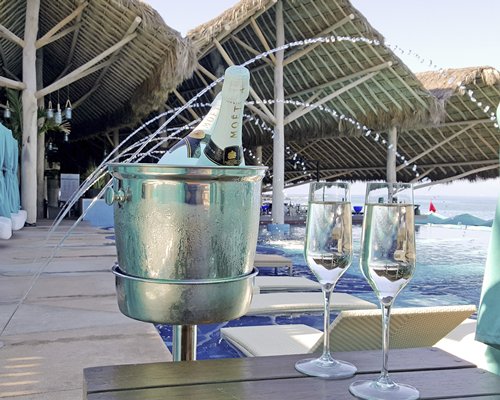 An outdoor swimming pool with chaise lounge chairs and wines on a table.