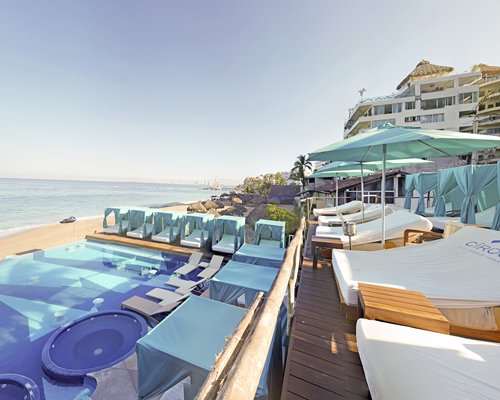An outdoor swimming pool and hot tub with cabanas alongside the ocean.