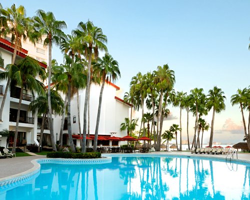 An outdoor swimming pool with sunshades and chaise lounge chairs alongside the resort units.