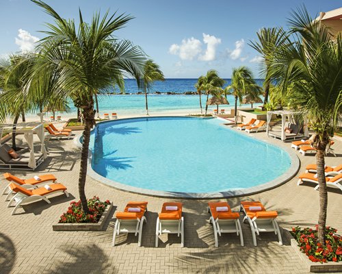 An outdoor swimming pool with chaise lounge chairs alongside the beach.
