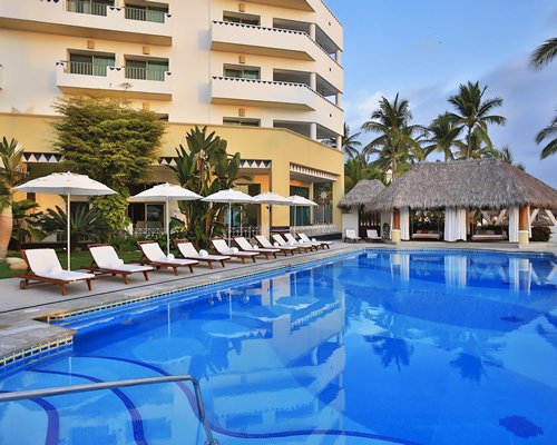 An outdoor swimming pool with lounge chairs and sunshades alongside multi story resort units.