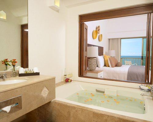 A bathroom with a bathtub and single sink vanity alongside a bedroom.