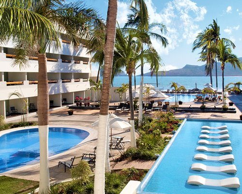 An outdoor swimming pool with chaise lounge chairs and sunshades alongside multi story units.