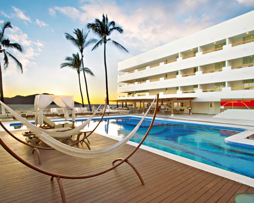 An outdoor swimming pool with chaise lounge chairs and hammocks alongside multi story units.