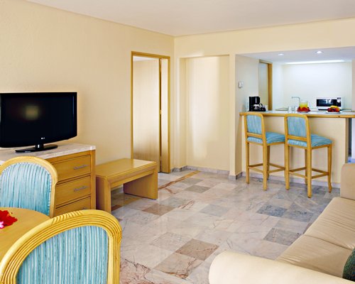 A well furnished living room with a television an open plan kitchen and dining area.