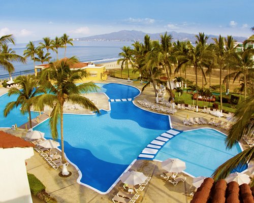 An outdoor swimming pool with chaise lounge chairs sunshades and palm trees alongside the pecan.
