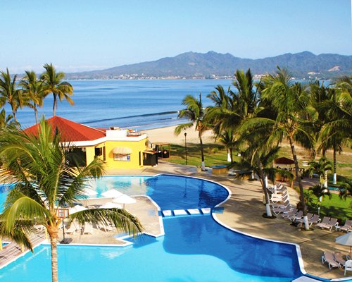 A scenic outdoor swimming pool with chaise lounge chairs and trees alongside the ocean.