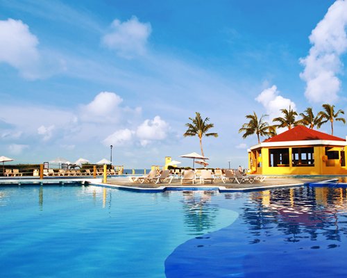 An outdoor swimming pool with chaise lounge chairs sunshades and a poolside bar.