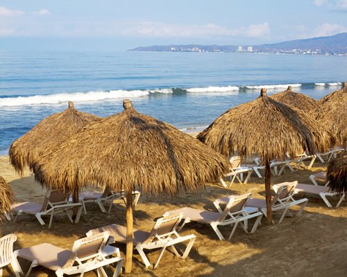 View of the beach with chaise lounge chairs and thatched sunshades alongside the ocean.