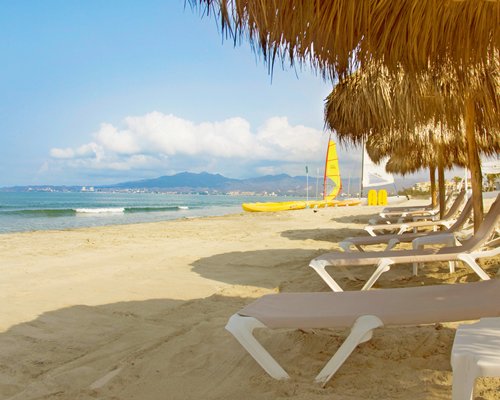 View of the beach with chaise lounge chairs thatched sunshades and boats.