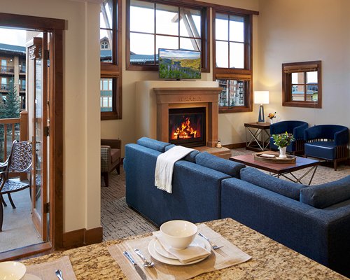 A well furnished living room with a television fire in the fireplace and an outside view.