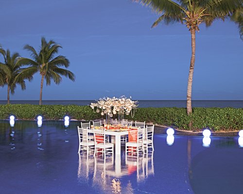 Outdoor swimming pool with dining area and palm trees alongside the ocean.