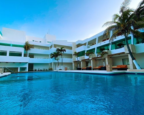 Outdoor swimming pool with chaise lounge chairs and palm trees alongside multiple balconies.