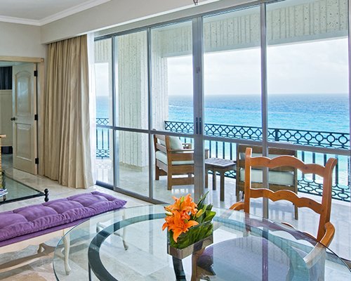 A well furnished living room with a television glass top dining table balcony and sea view.