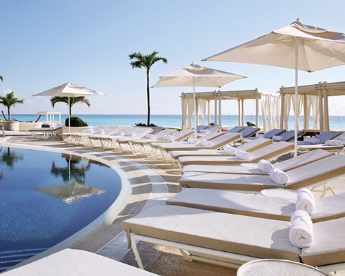 An outdoor swimming pool with chaise lounge chairs sunshades and cabana.