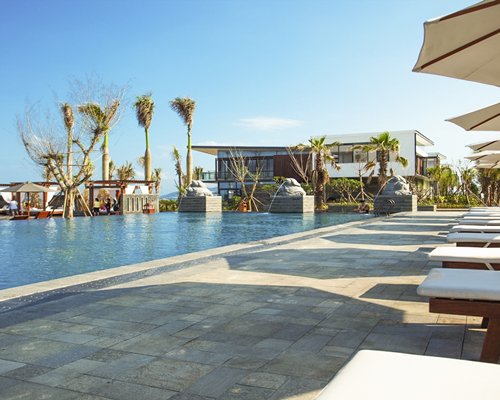 An outdoor swimming pool with chaise lounge chairs sunshades and water fountain.