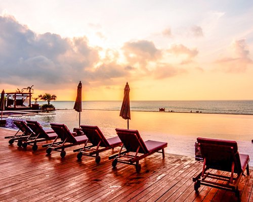 An outdoor swimming pool with chaise lounge chairs and sunshades at dusk.