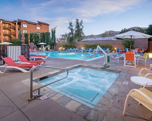 An outdoor swimming pool with hot tub chaise lounge chairs and sunshades alongside the resort unit.