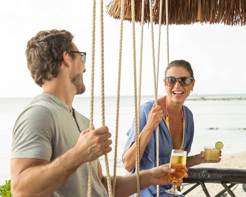 Outdoor swimming pool with chaise lounge chairs and thatched sunshades alongside the sea.