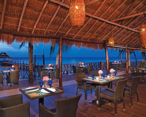 An outdoor restaurant alongside a wooden pier leading to the ocean.
