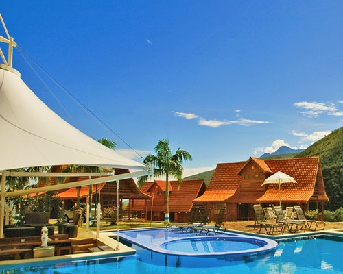 An outdoor swimming pool with a hot tub and chaise lounge chairs alongside multiple resort units.