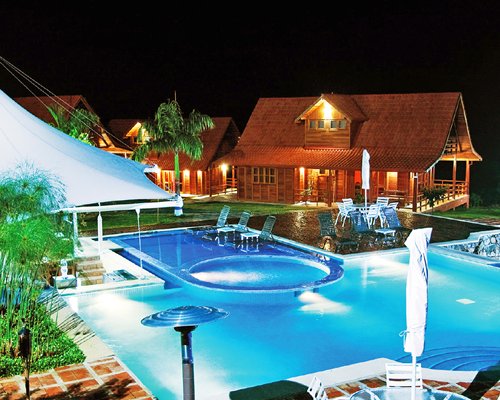 An outdoor swimming pool with a hot tub alongside the resort at night.