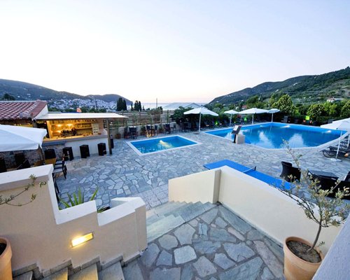An outdoor swimming pool and hot tub with chaise lounge chairs at dusk.