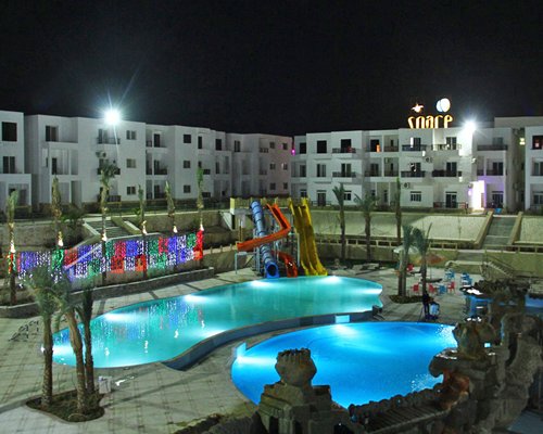 An exterior view of resort and pools with lights at night.